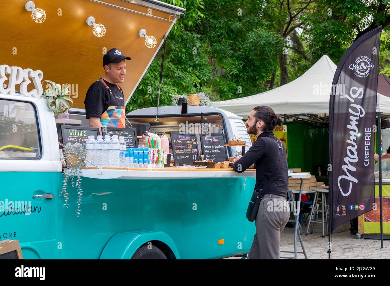 Hombre joven haciendo un pedido en una furgoneta de comida volkswagen T2 en el Festival de Dinosaurios en la ciudad de Katerini, Grecia Foto de stock