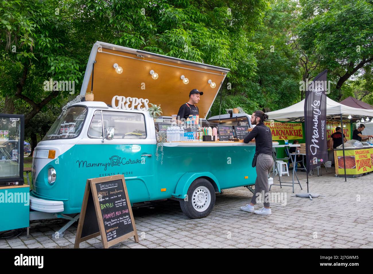 Un hombre de mediana edad pidiendo su café en una furgoneta Volkswagen T2 de café en el Festival de Dinosaurios en la ciudad de Katerini, Grecia Foto de stock