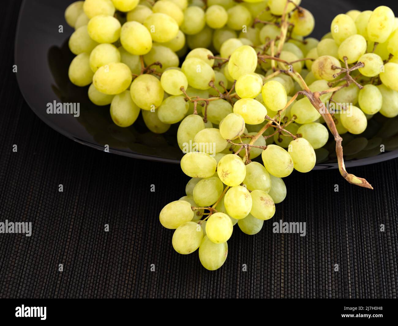 Una manada de uvas Sultanas sobre un plato negro. Fondo negro servilleta Foto de stock