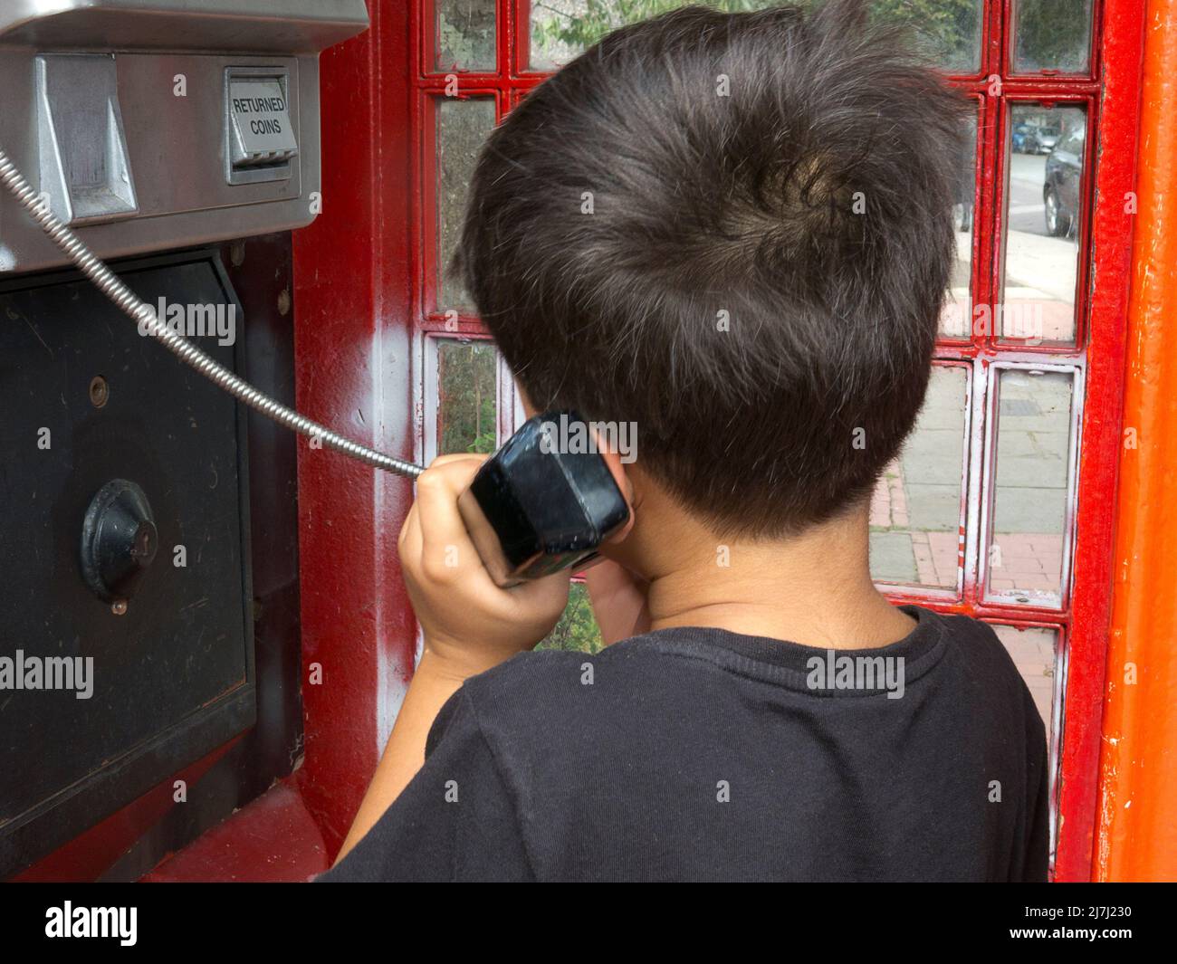 niño pequeño en la caja de teléfono pública Foto de stock