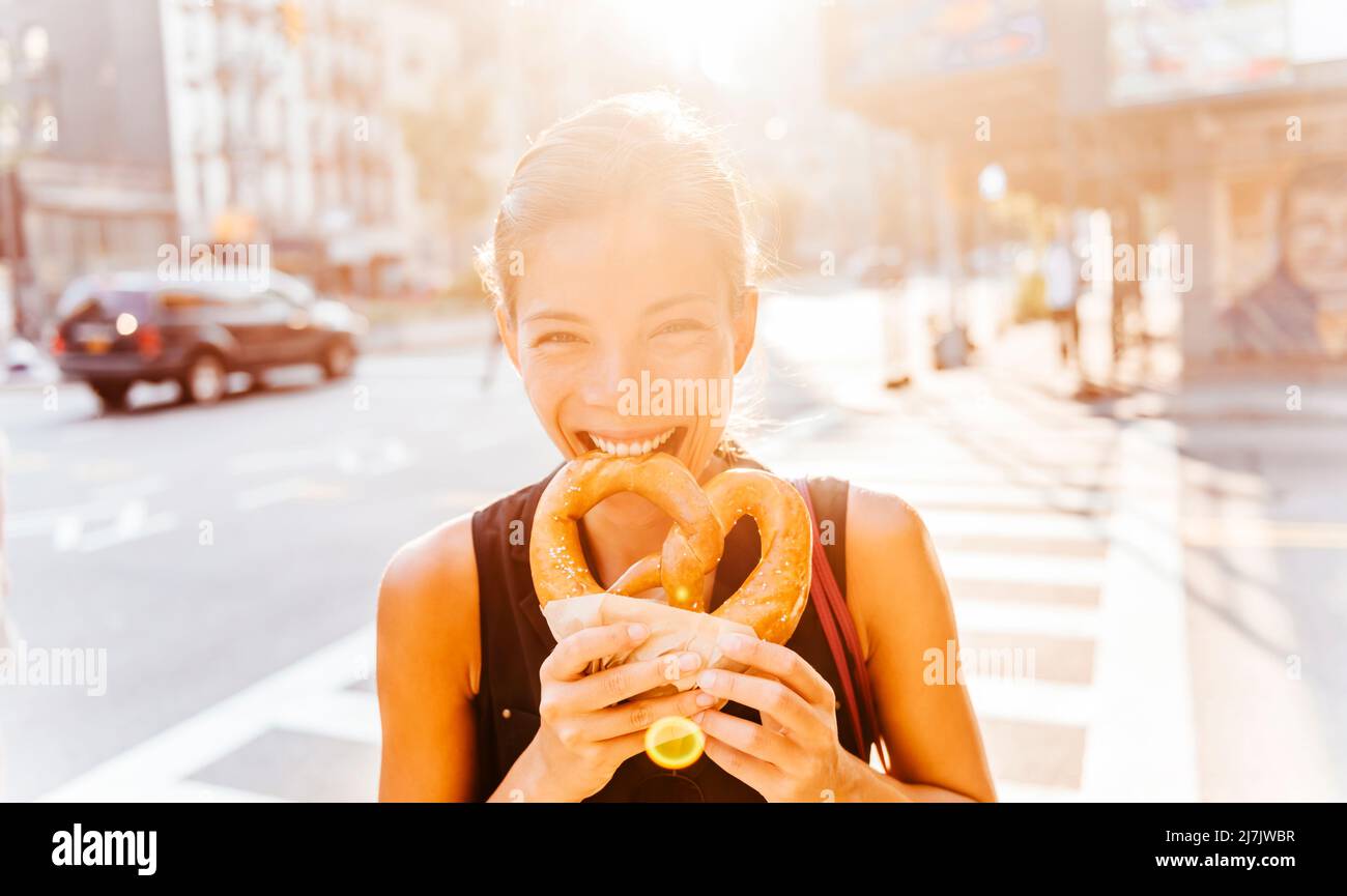 Mujer comiendo pretzel en Manhattan, un clásico bocadillo de la ciudad de Nueva York. Retrato profesional joven asiático multirracial sonriendo en la cámara Foto de stock