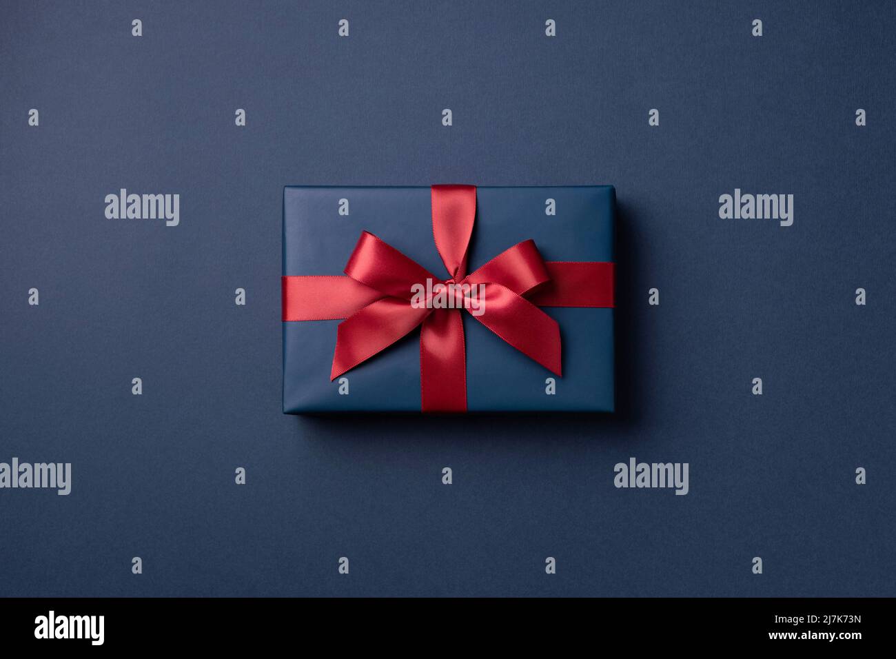 Caja de regalo azul con cinta roja sobre fondo azul oscuro. Foto de stock