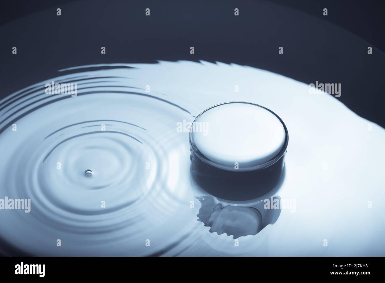 Imagen minimalista de un vaso de agua con gotas caídas sobre la superficie del agua. Imagen abstracta del agua en blanco y negro. Foto de stock