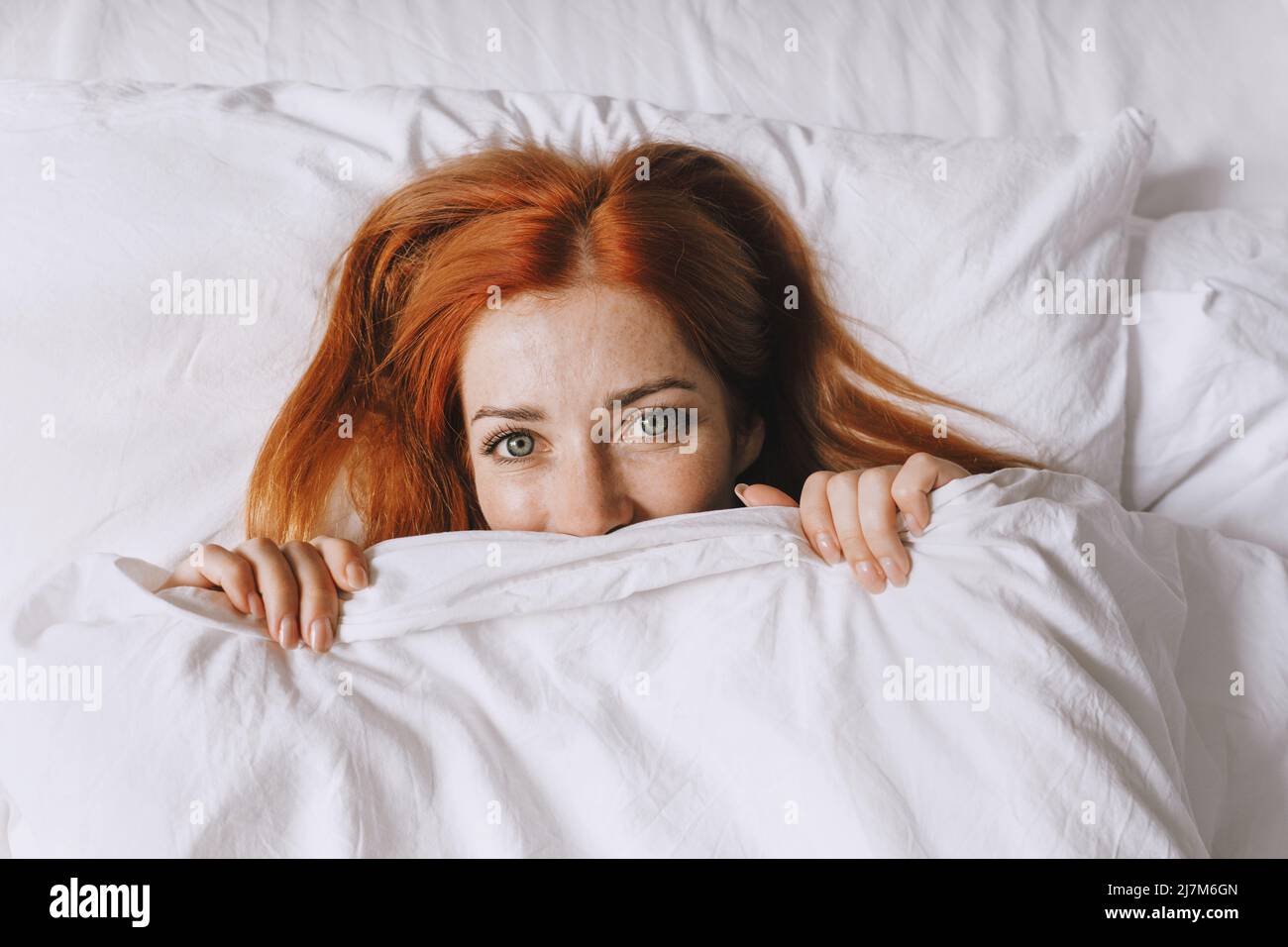 mujer joven coy escondida bajo la cubierta de la cama Foto de stock