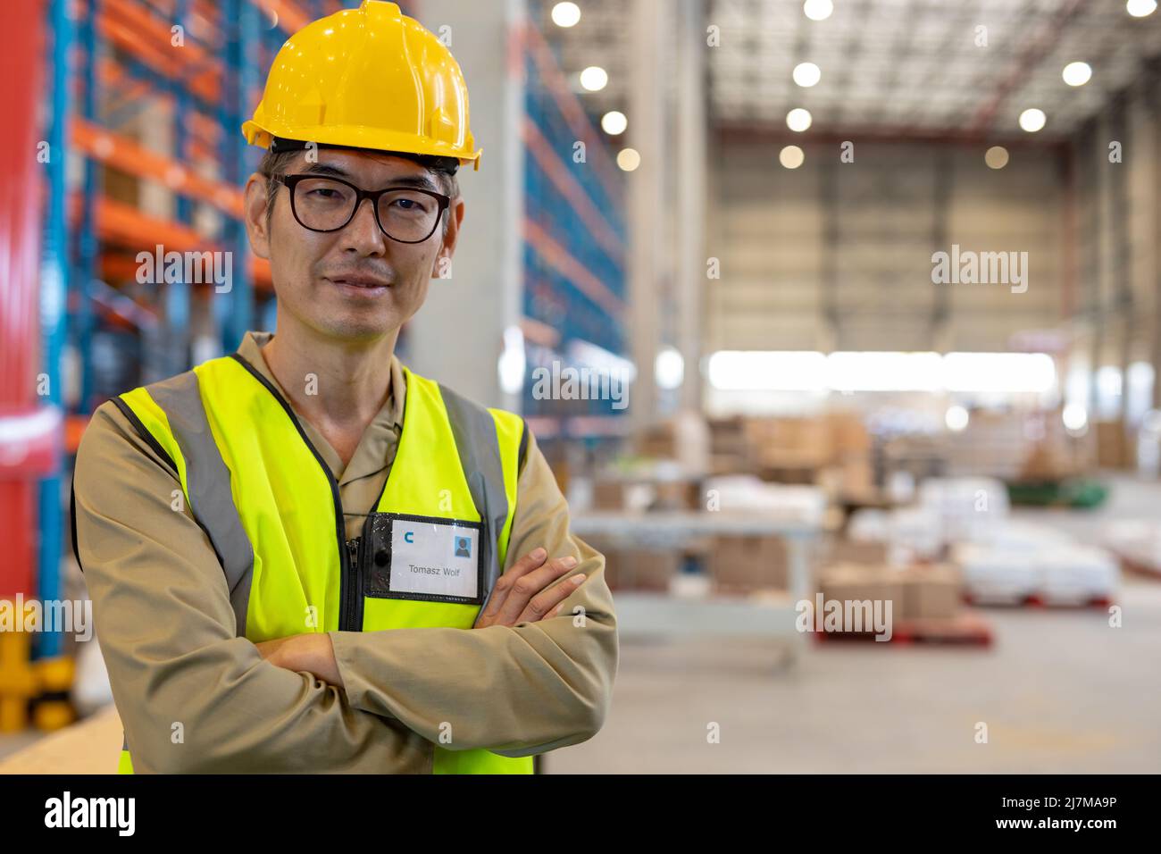 Retrato de un trabajador asiático maduro seguro con brazos cruzados llevando chaleco reflectante y casco Foto de stock