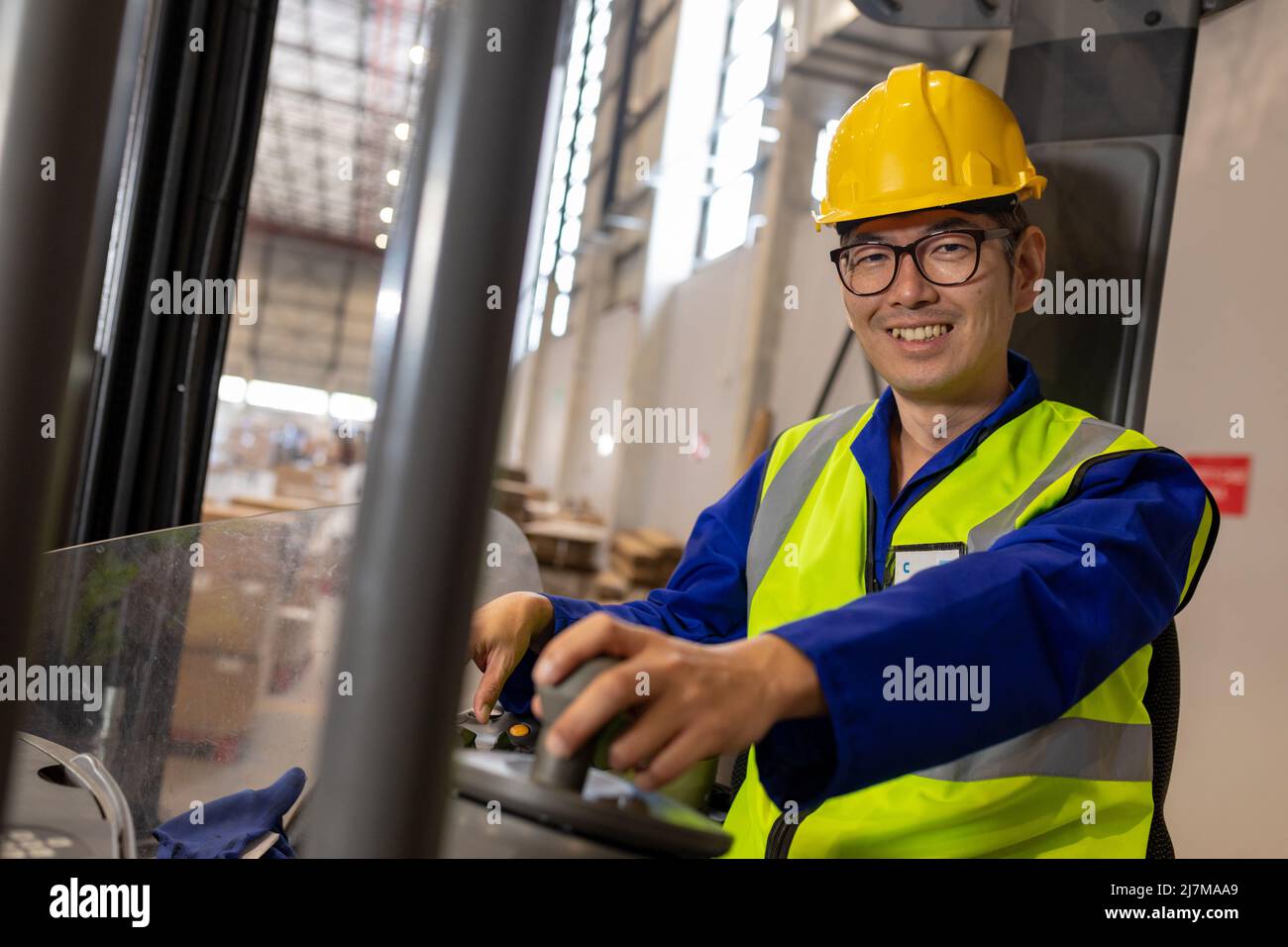 Retrato de un trabajador asiático maduro sonriente con chaleco reflectante y carretilla elevadora de conducción con casco Foto de stock
