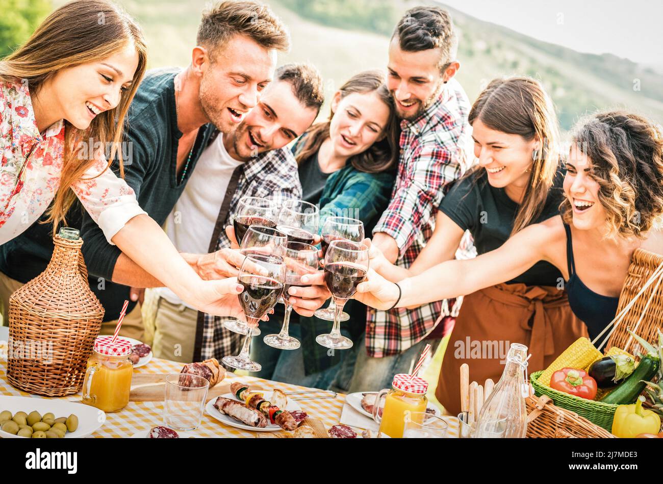 Jóvenes amigos que se divierten al aire libre tostar vino tinto en la fiesta al aire libre bar-b-q - Feliz gente comiendo comida a la parrilla en la bodega granja - Foto de stock