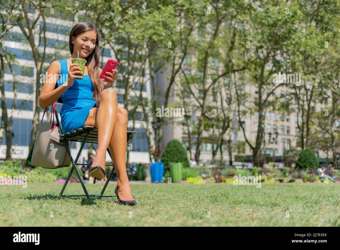 Bryant Park, Manhattan, Nueva York. Jóvenes profesionales multiculturales que beben jugo de batido verde con la aplicación del teléfono en verano Foto de stock