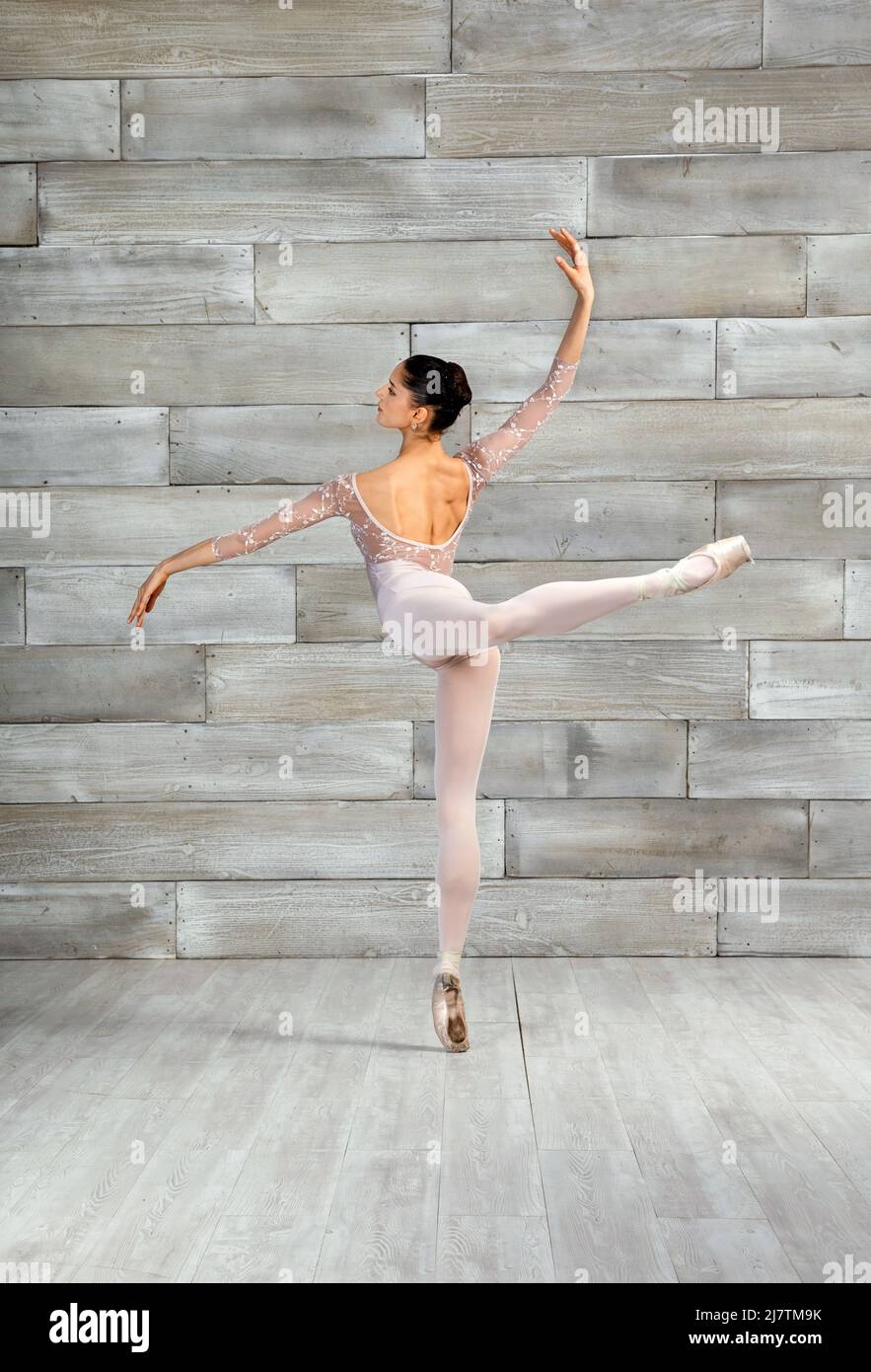 Vista posterior del cuerpo completo de bailarina de ballet flexible con actitud Pose con la pierna elevada mientras baila en un estudio ligero Foto de stock