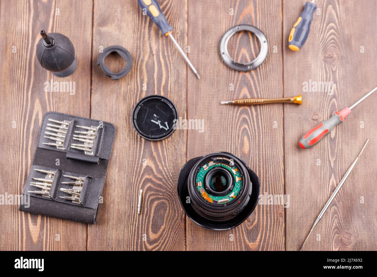 lente de zoom de cámara medio desmontada sobre mesa de madera rodeada de herramientas Foto de stock