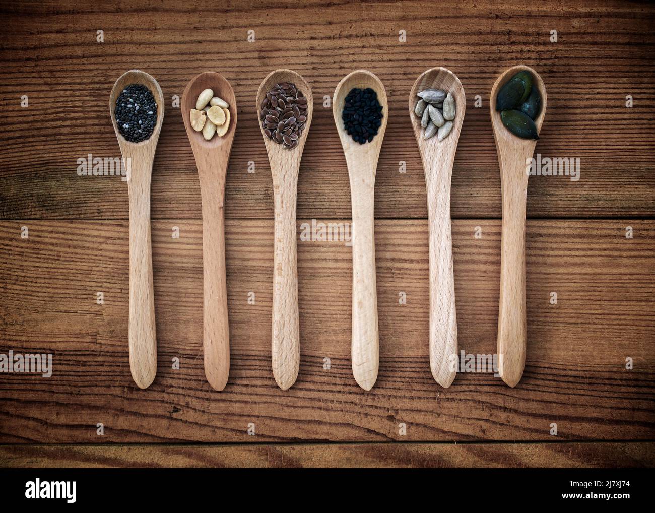Conjunto de semillas orgánicas en cucharas sobre fondo de madera, alimentos naturales saludables y concepto de nutrición Foto de stock