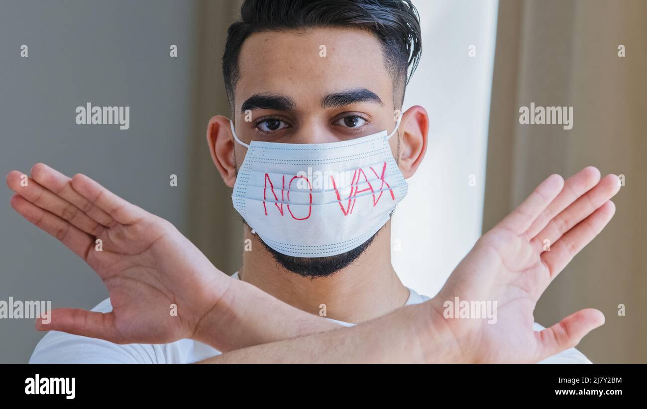 Retrato del hombre árabe hispano en máscara médica protectora con inscripción ninguna vacuna cruza los brazos delante de él negándose a manifestarse protesta Foto de stock