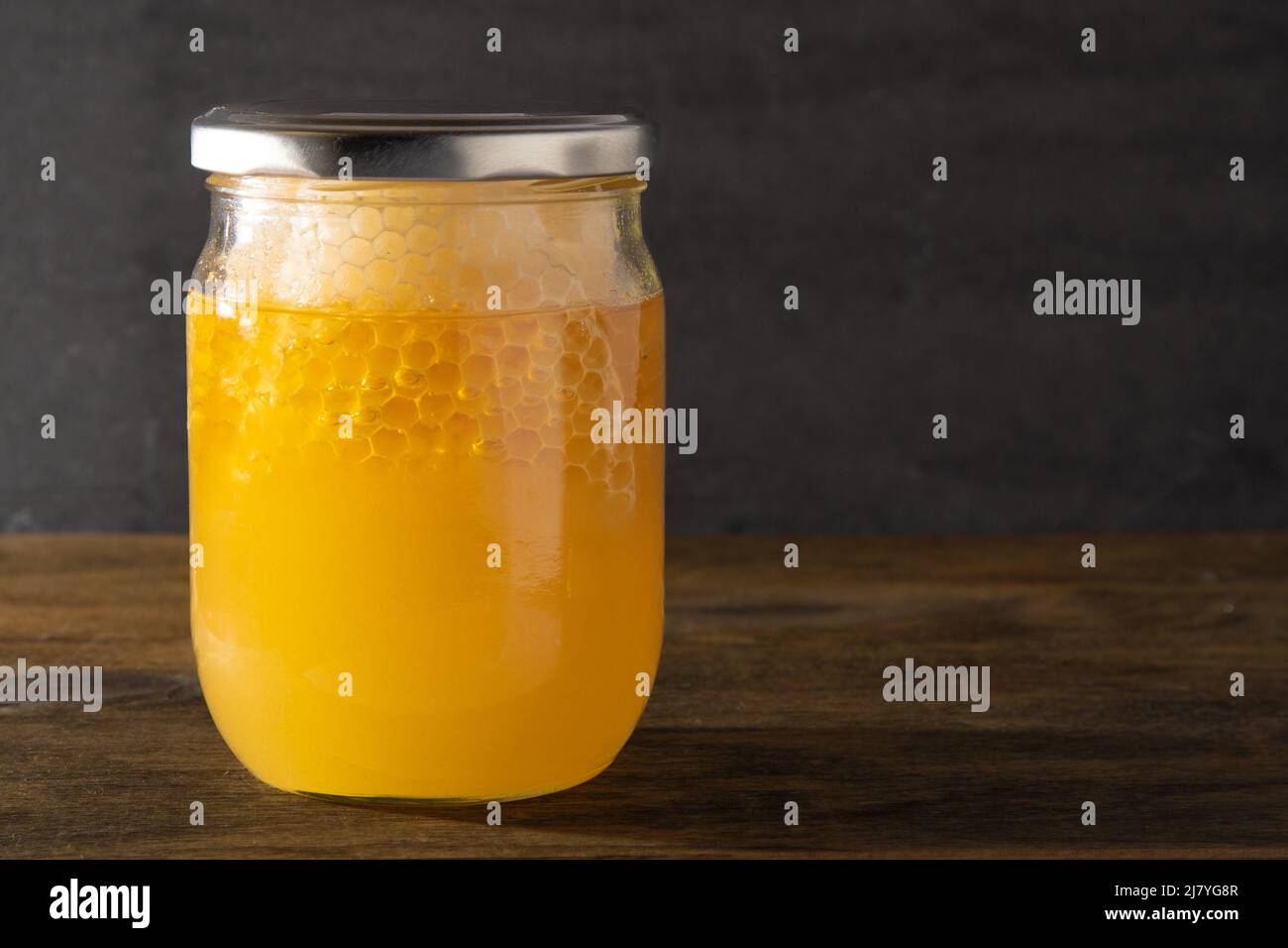 Tarro de miel con panales. Producto de abeja transparente amarilla. Embalaje de medio litro con espacio para una etiqueta. Fondo de madera. Miel de abeja en una jarra de cristal. Alimentos naturales saludables. Espacio de copia. Foto de stock