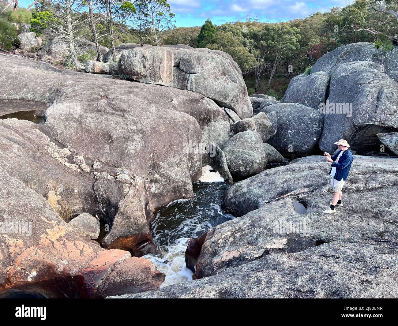 Hombre fotografiando Bald Rock Creek cerca de Wave Rock en Underground Creek, Parque Nacional Girraween, Queensland, Australia Foto de stock