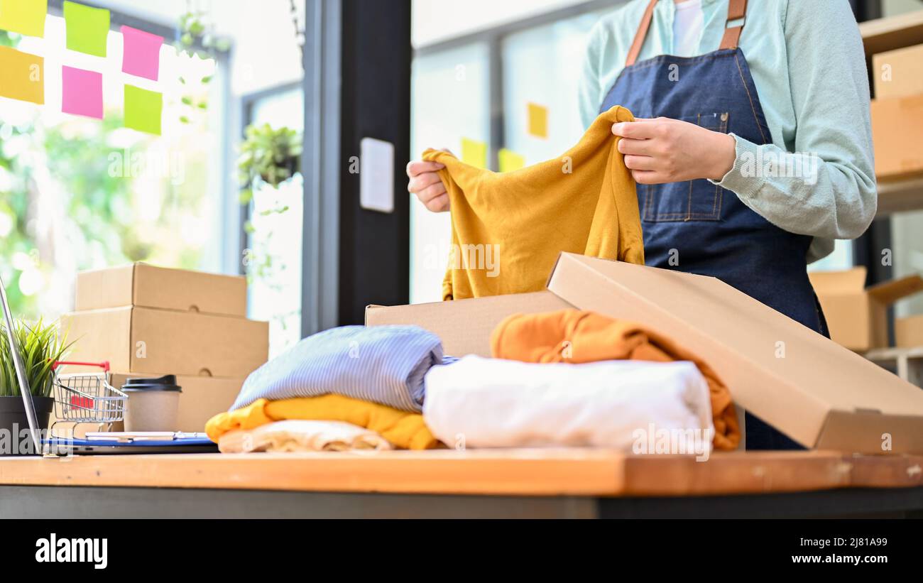 Ropa plegable femenina, preparando su paquete de productos de moda para enviar a sus clientes. Concepto de negocio de inicio de moda. Imagen recortada Foto de stock