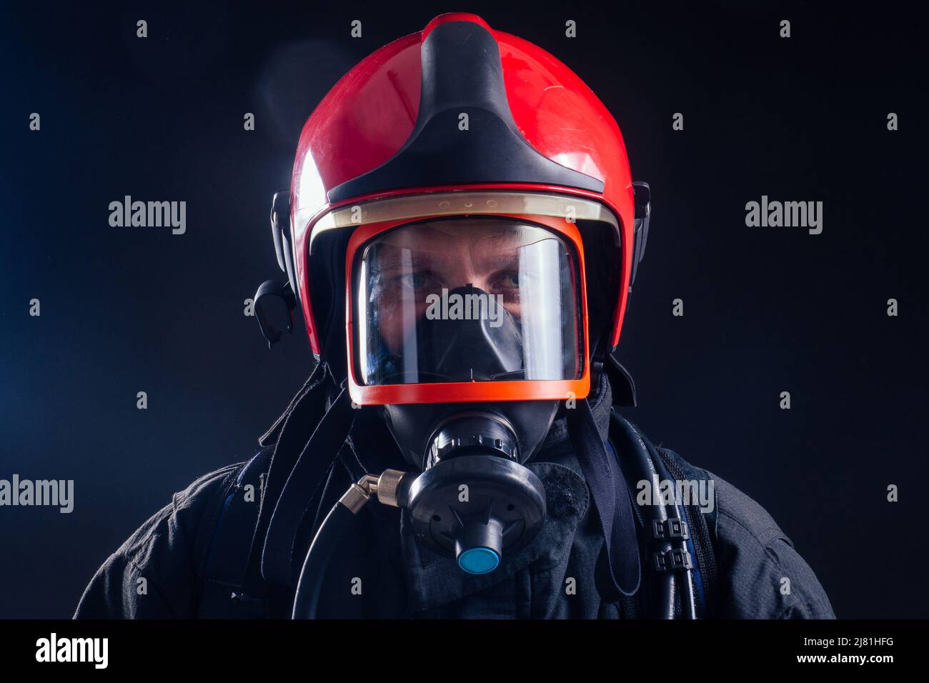 retrato fuerte bombero en uniforme a prueba de fuego sosteniendo un hacha chainsaw en sus manos negro fondo studio.oxygen máscara en la cabeza cerca Foto de stock