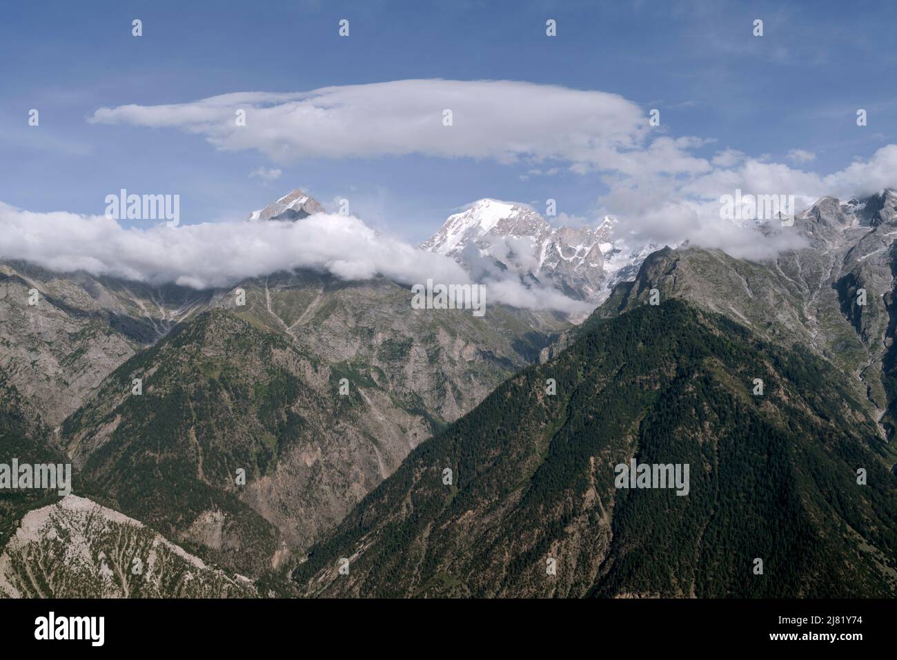 Montañas del Himalaya con picos nevados, escarpadas pendientes, algunas con bosques, todas bajo cielo azul brillante con formas de nubes vistas desde Kalpa, India. Foto de stock
