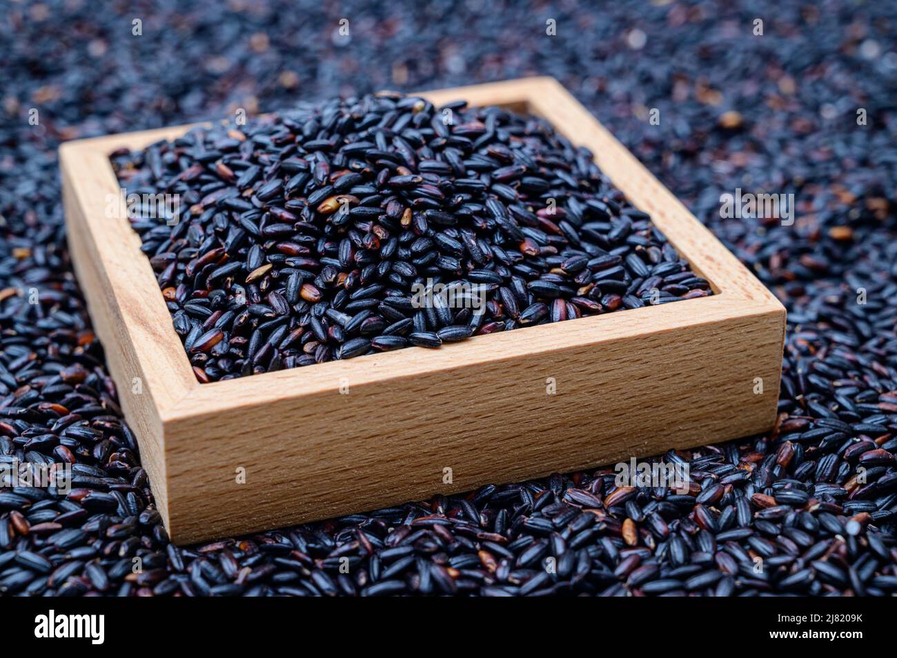 Un fondo con arroz negro apilado y un tazón de madera que contiene arroz negro. Foto de stock