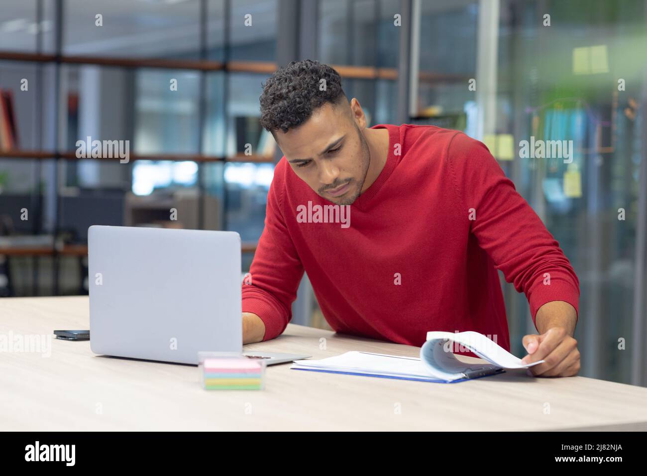 Consejero masculino hispano analizando el documento mientras está sentado con el ordenador portátil en un lugar de trabajo moderno Foto de stock