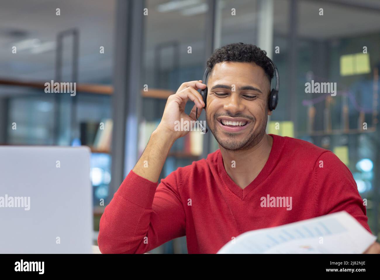 Sonriente telecaladora masculina hispana hablando a través del auricular en un lugar de trabajo moderno Foto de stock