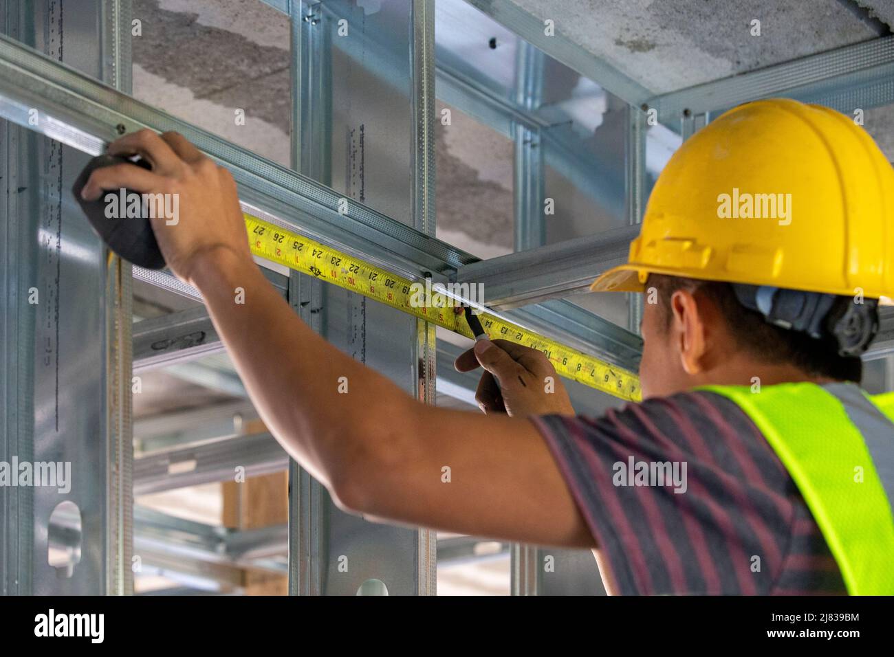 un trabajador de la construcción experto, trabajando como un framer está midiendo algunos puntales de apoyo estructural para agregar a la integridad estructural del buidoutl Foto de stock