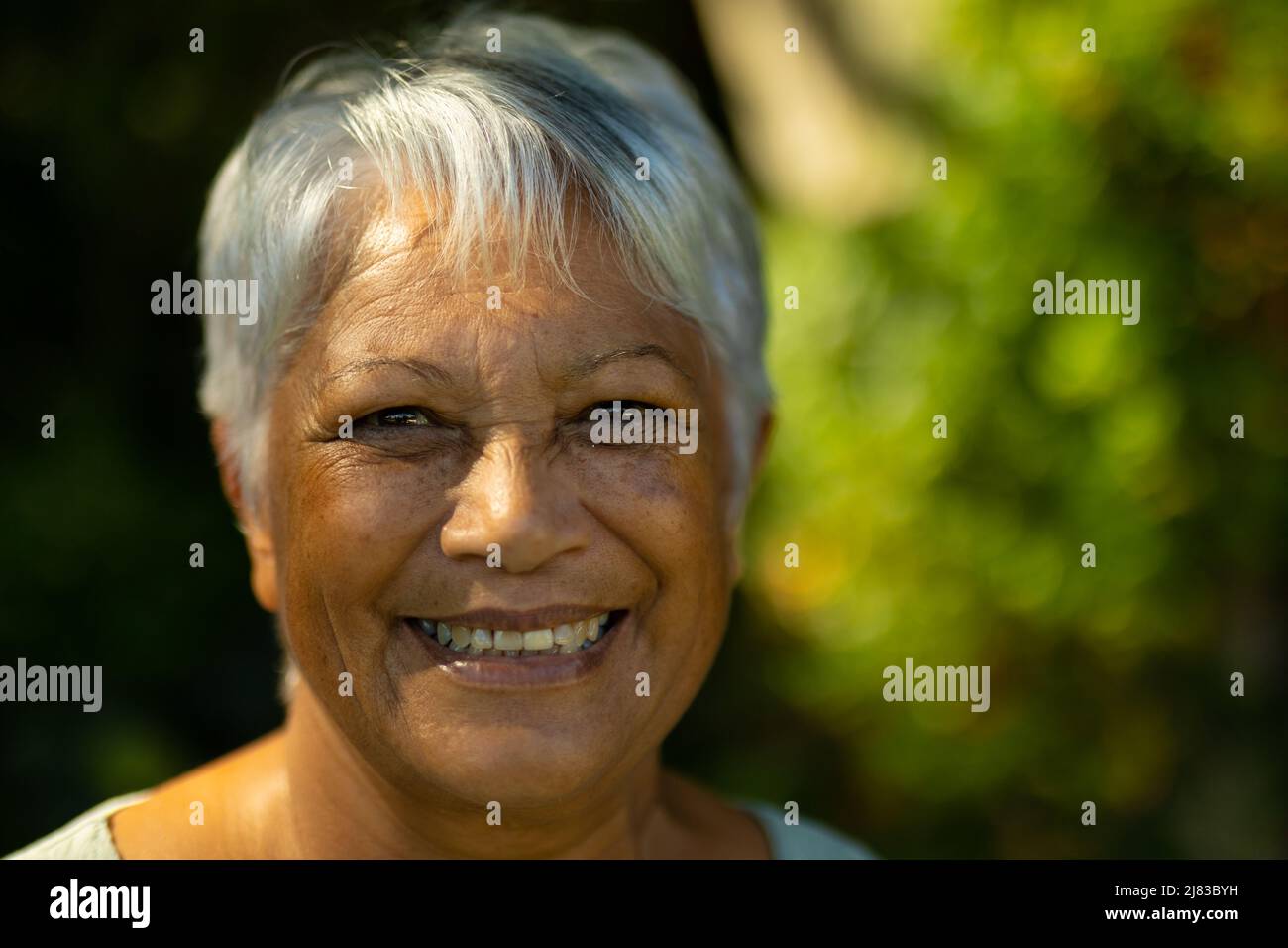 Primer plano retrato de una mujer mayor biracial sonriente con pelo gris corto en el parque Foto de stock