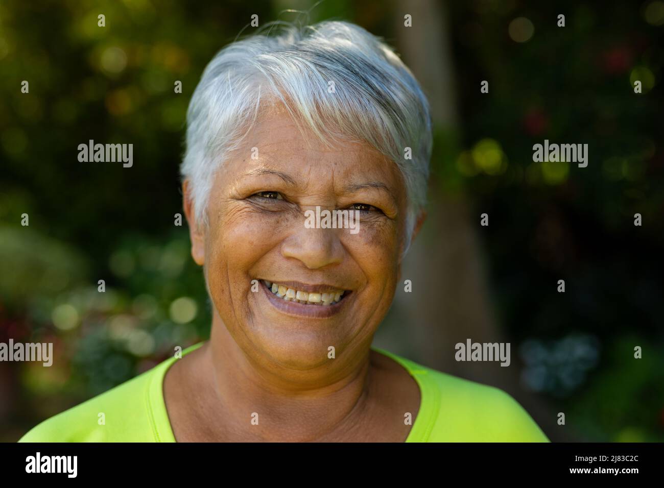 Primer plano retrato de una mujer mayor biracial sonriente con pelo gris corto en el patio Foto de stock