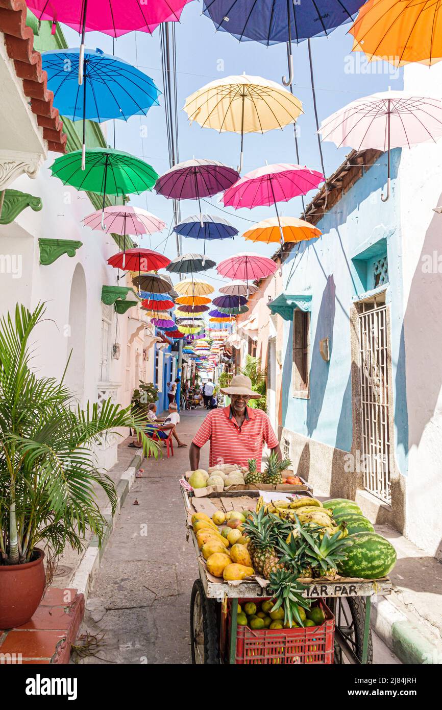 Cartagena COLOMBIA,Getsemani Callejon Angosto Calle 27 Colgantes paraguas coloridos,vendedor de frutas callejero callejero hispano empujando carro hombre hombre Foto de stock