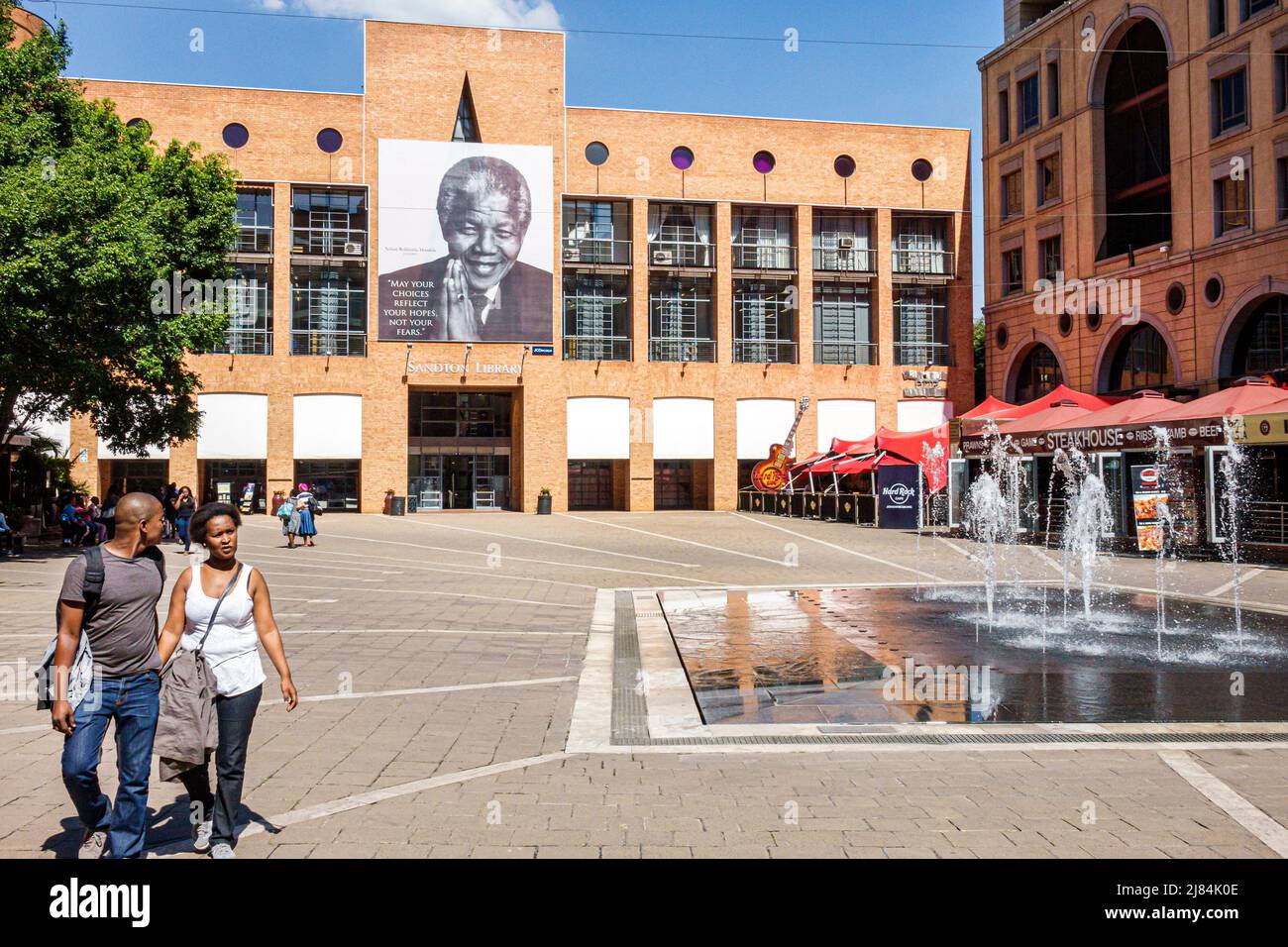 Johannesburgo Sudáfrica, Sandton, Nelson Mandela Square, fuente pública, hombre negro masculino, mujer pareja femenina, Sandton Library Foto de stock