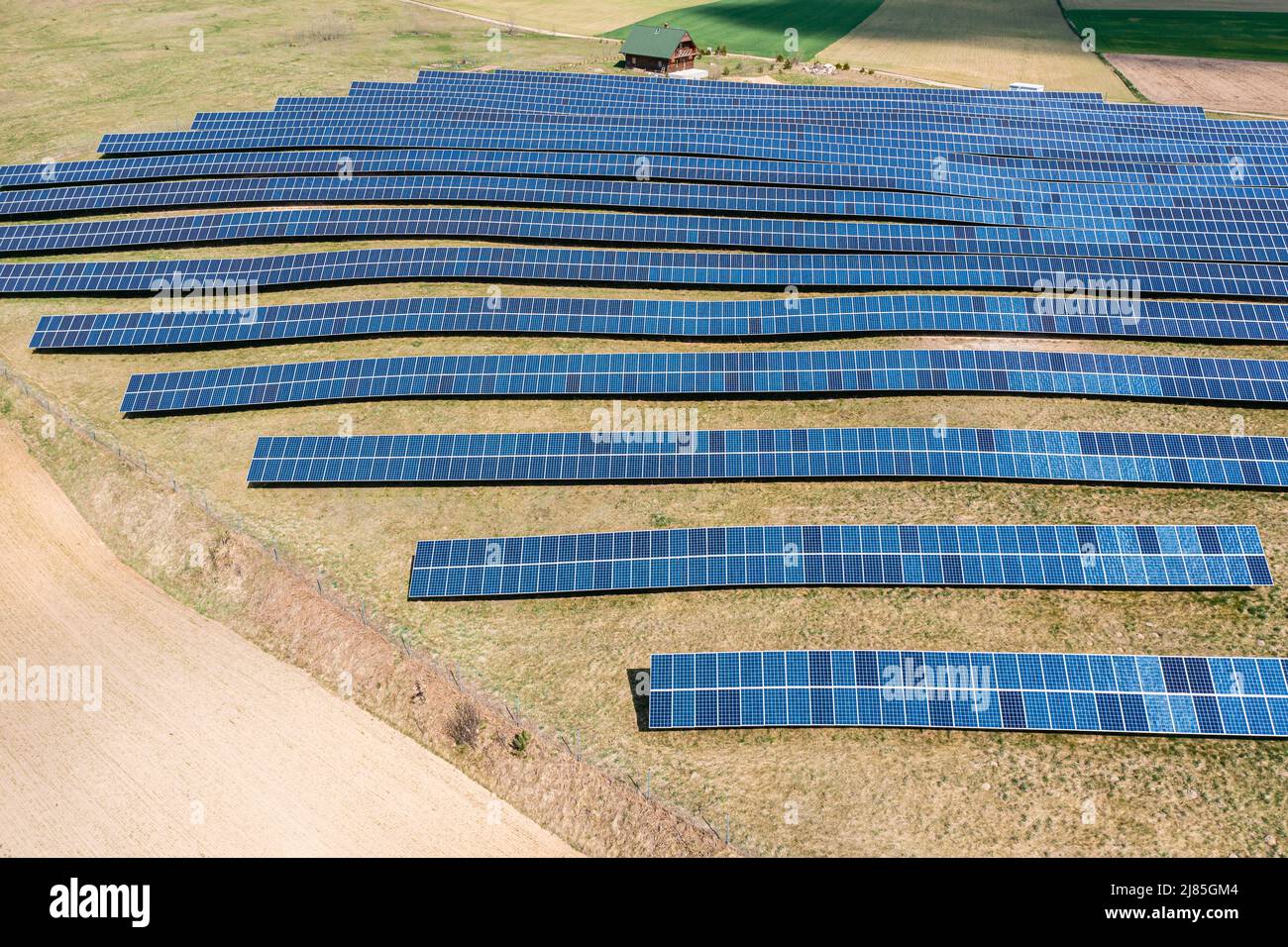 Vista aérea de la granja solar, filas de paneles fotovoltaicos por una pequeña casa Foto de stock