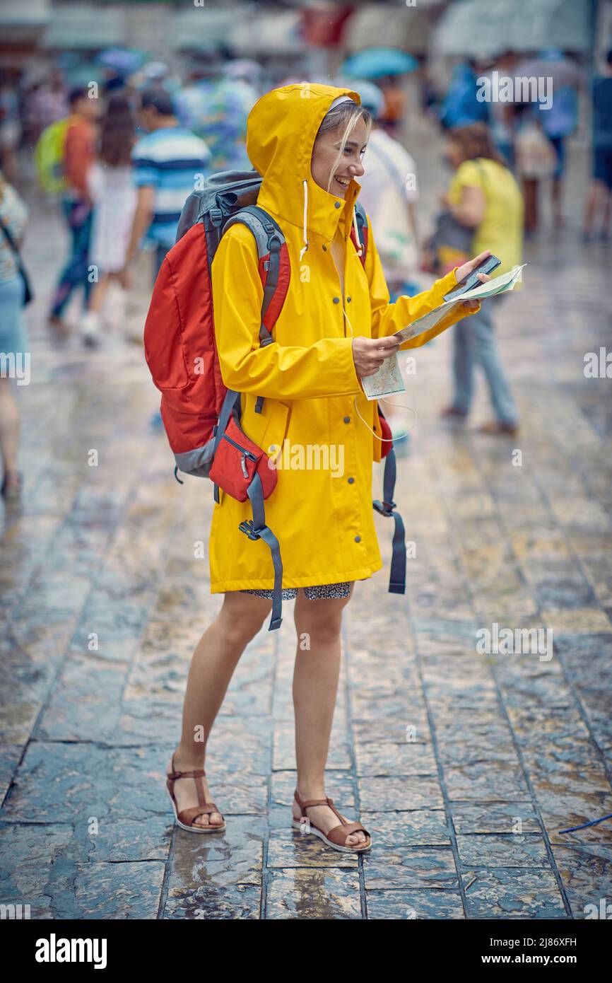 Mujer de turismo en raincoat, con mapa y teléfono en la ciudad a pie. Lluvia de verano. Concepto de viaje y estilo de vida. Foto de stock