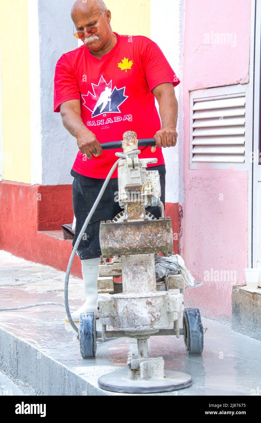Un cubano afrocaribeño opera un equipo de pulido rústico y casero. Está puliendo la acera de granito en la nueva oficina de viajes de El Ra Foto de stock