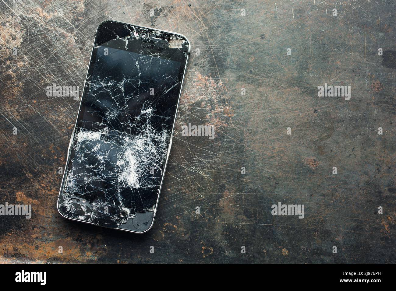 Smartphone muy dañado con carcasa metálica doblada y cristal roto sobre fondo de grunge. Primer plano. Foto de stock