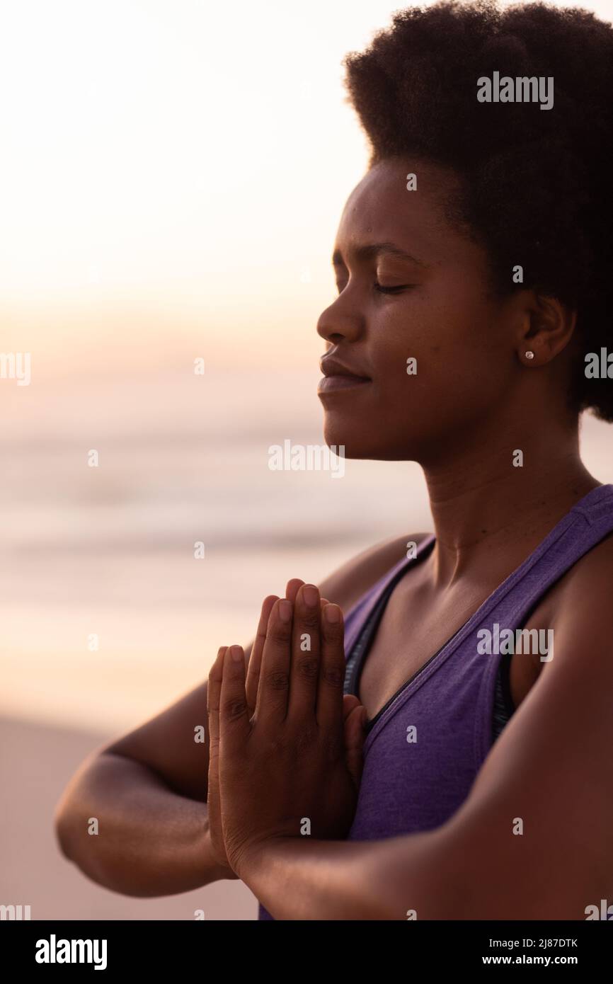 Primer plano de una mujer madura afroamericana con ojos de pelo afro que cierran y meditan en la playa Foto de stock