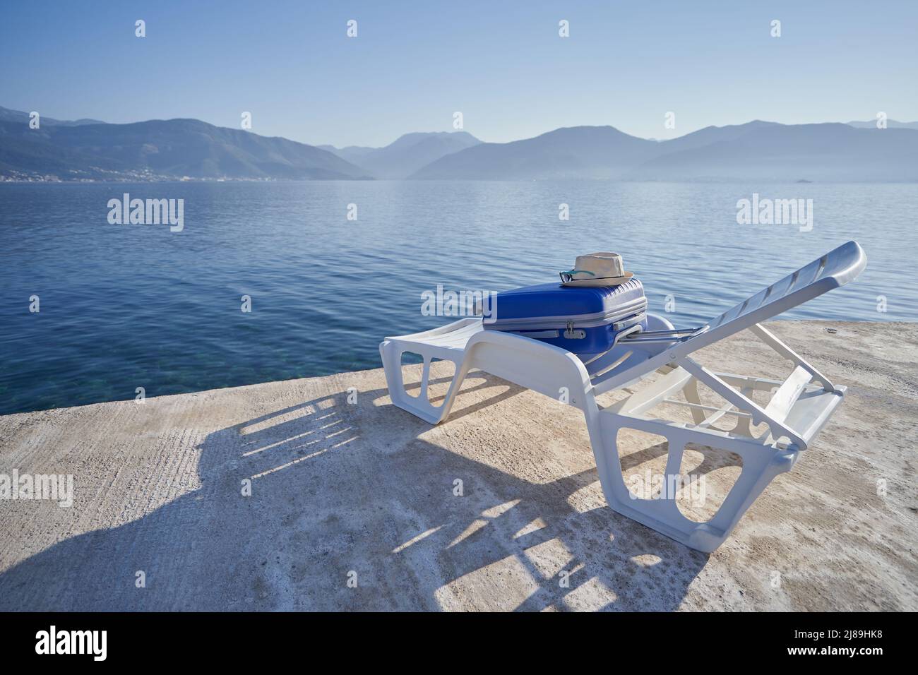La maleta azul se encuentra en una silla de playa junto al mar, concepto de viaje Foto de stock