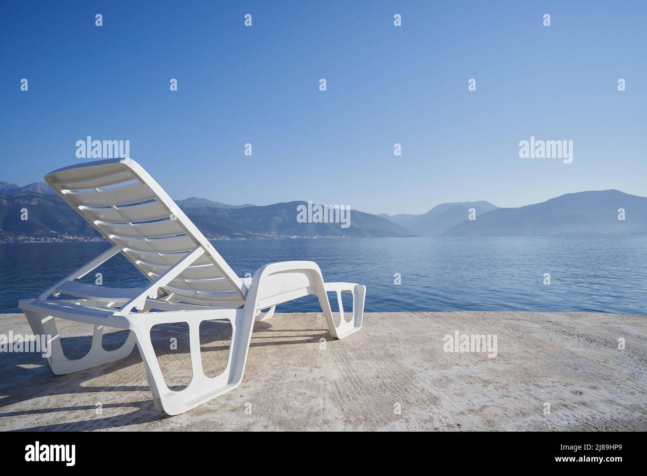 Silla de playa de plástico contra el mar y las montañas, concepto de viaje Foto de stock