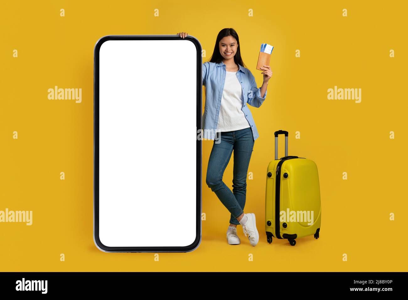 Alegre joven dama asiática en informal con la maleta muestra pasaporte, el  billete de avión está cerca de un teléfono enorme Fotografía de stock -  Alamy