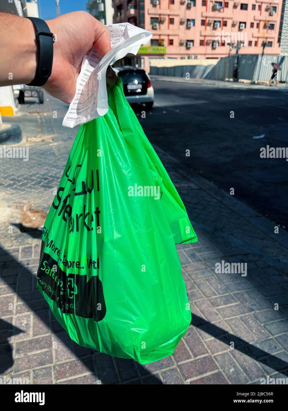 La mano de un hombre sostiene una bolsa de compras y un cheque de caja contra el telón de fondo del distrito pobre. Foto de stock