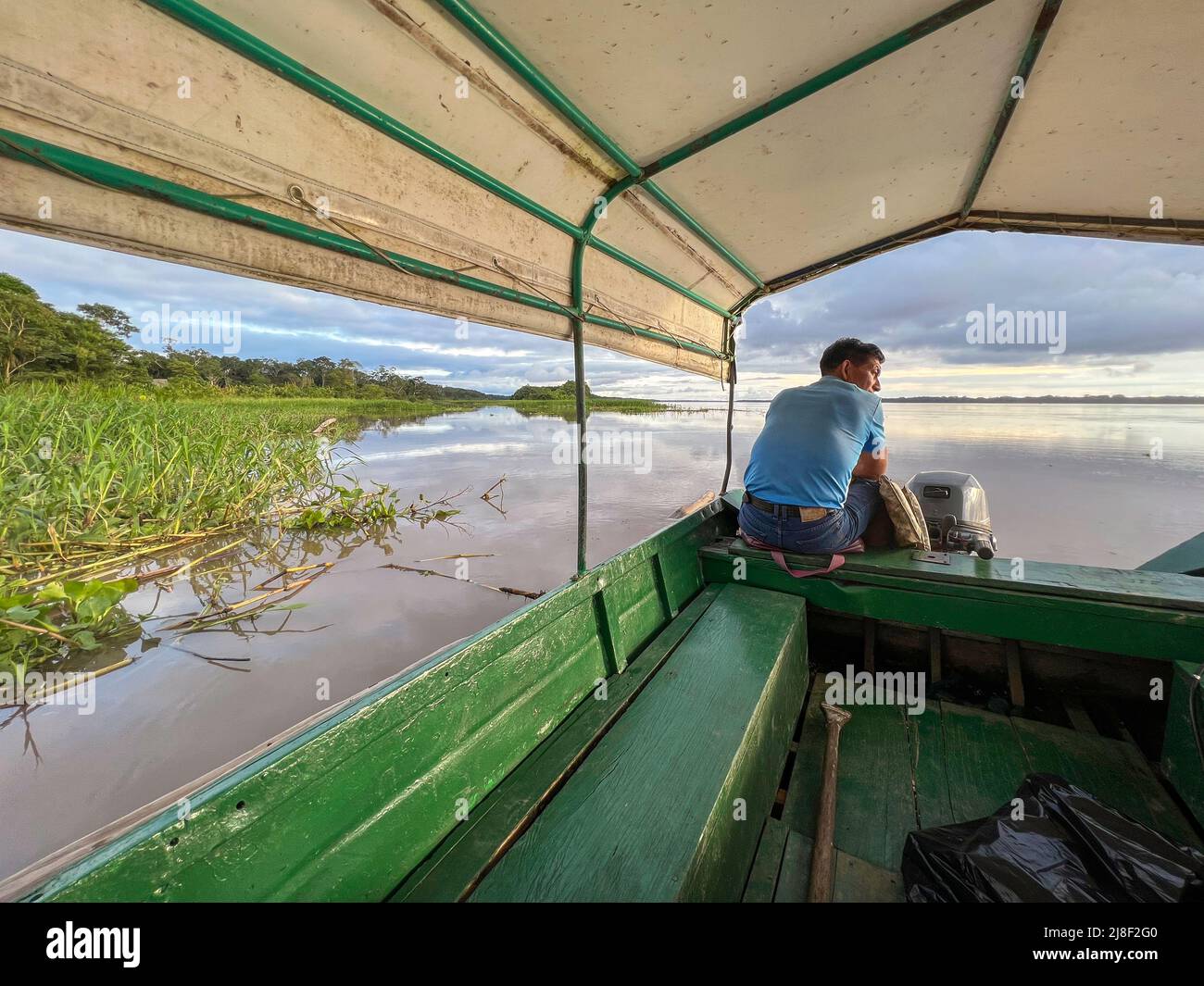 Guía turístico local navegando por un barco cubierto de madera en el río Amazonas en Perú Foto de stock