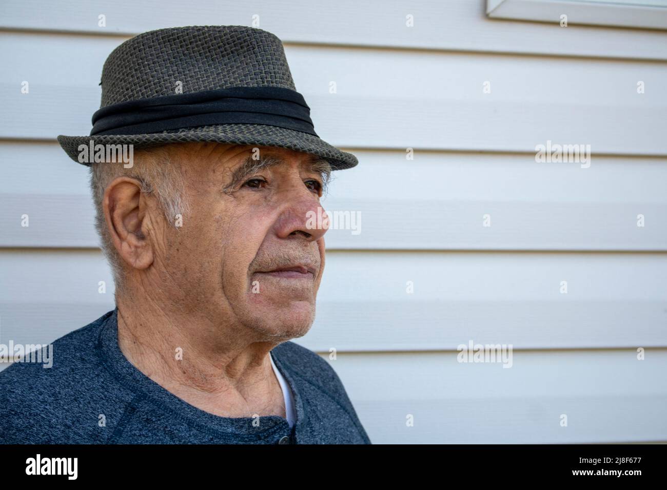 adulto mayor de sexo masculino caucásico con un sombrero fedora delante de una pared exterior blanca de la casa Foto de stock