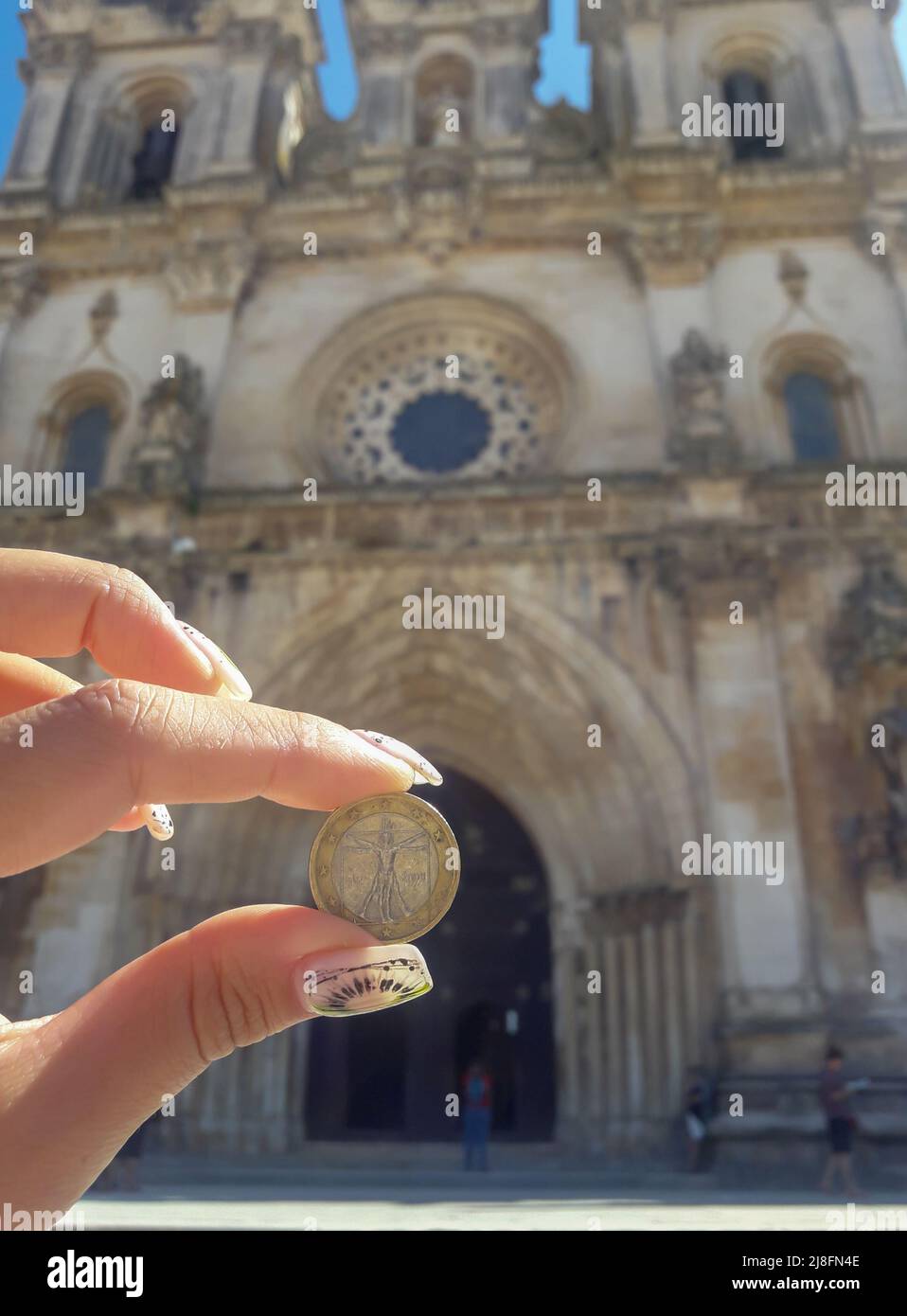 Mano sosteniendo una moneda con la imagen del Hombre Vitruviano en el fondo de un edificio antiguo Foto de stock