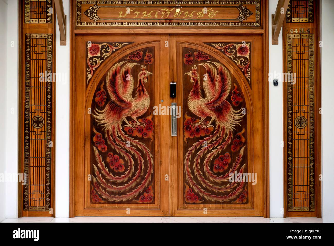 Detalle de puerta de madera tallada con figuras de pollo gallo con un impresionante plumaje de Tailandia en el sudeste asiático Foto de stock