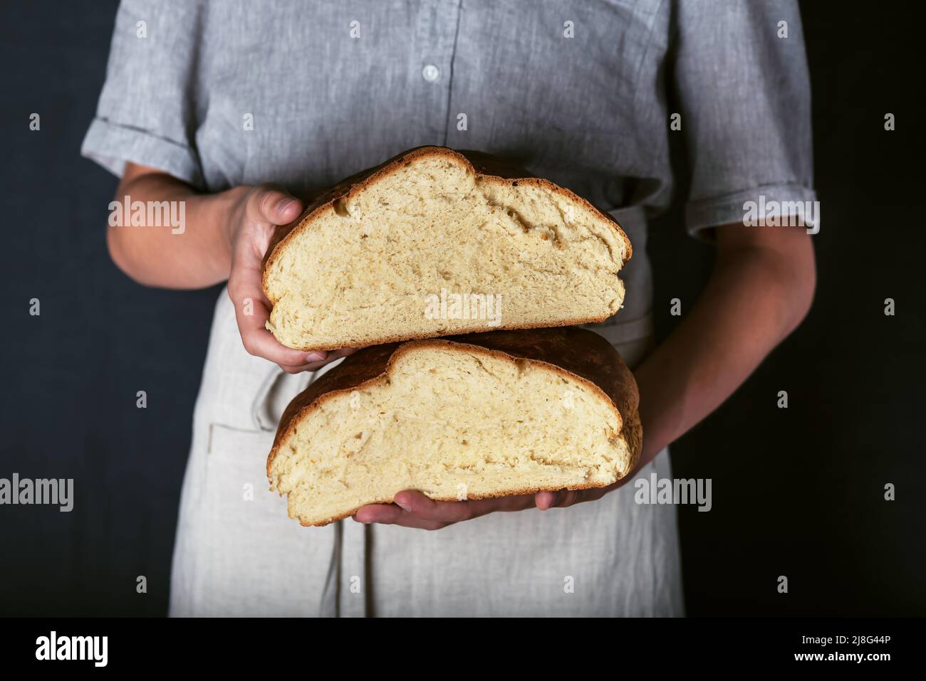 Manos femeninas sosteniendo pan artesano de masa de harina recién horneado rebanado en medias. Casero con harina de trigo y entrante. Estilo rústico oscuro. Foto de stock