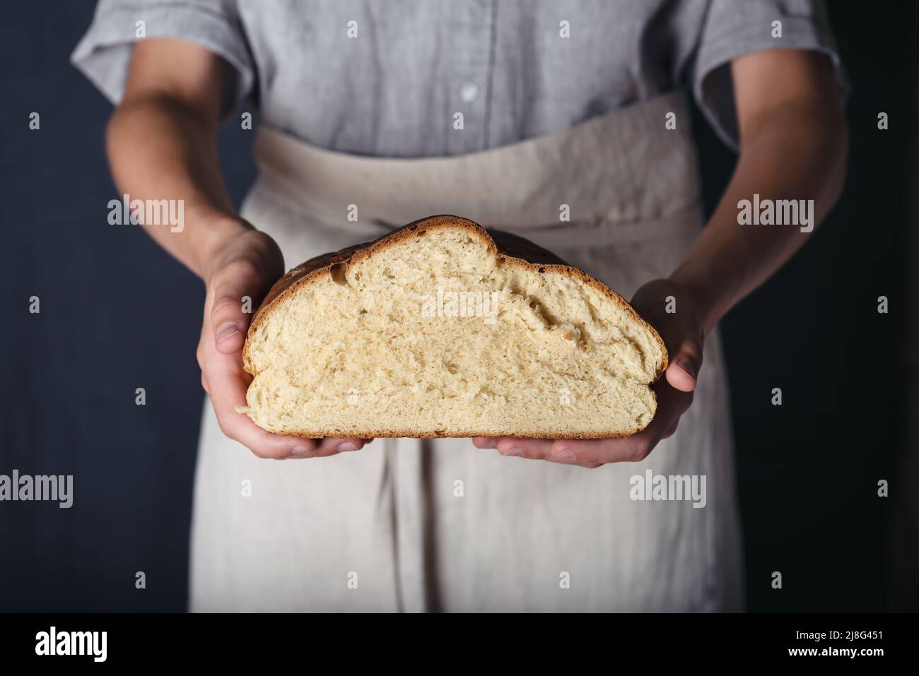 Manos femeninas sosteniendo medio pan casero recién horneado. Sin gluten, concepto de dieta saludable. Estilo rústico oscuro. Foto de stock