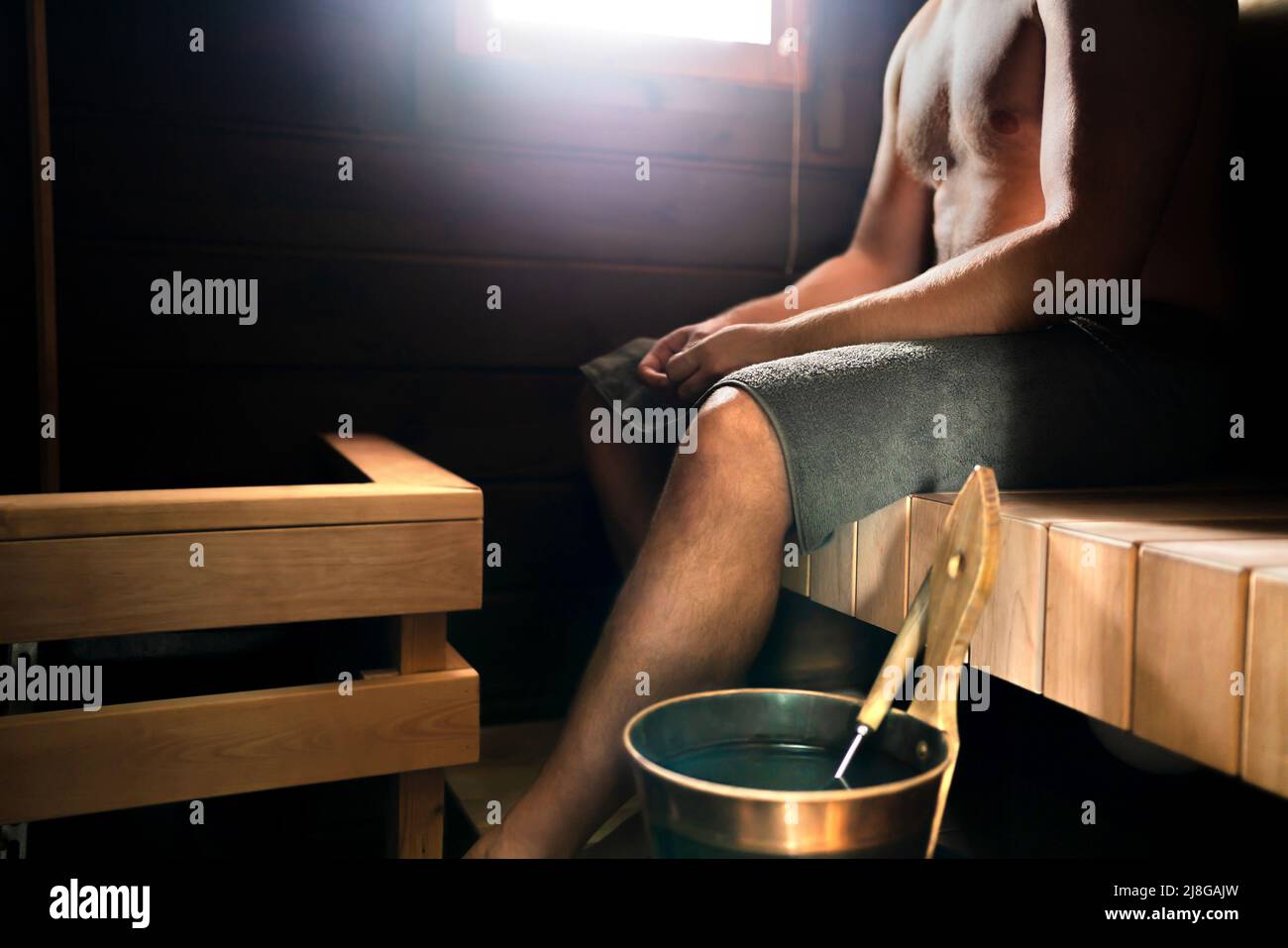 Sauna en Finlandia. Hombre que se relaja en la sala de vapor en el spa, la cabaña, la casa o el hotel de bienestar. Verano tradicional finlandés. Interior de madera antigua. Cubo de agua. Foto de stock