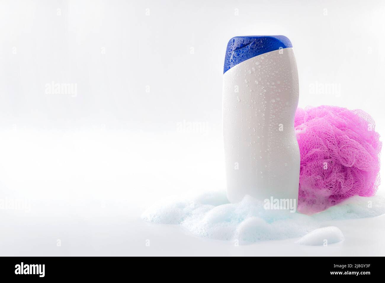 Higiene personal y cuidado del cuerpo artículos de tocador tema concepto con una botella de gel de ducha empapado en gotas de agua, burbujas hechas por espuma de jabón y ducha de color rosa Foto de stock
