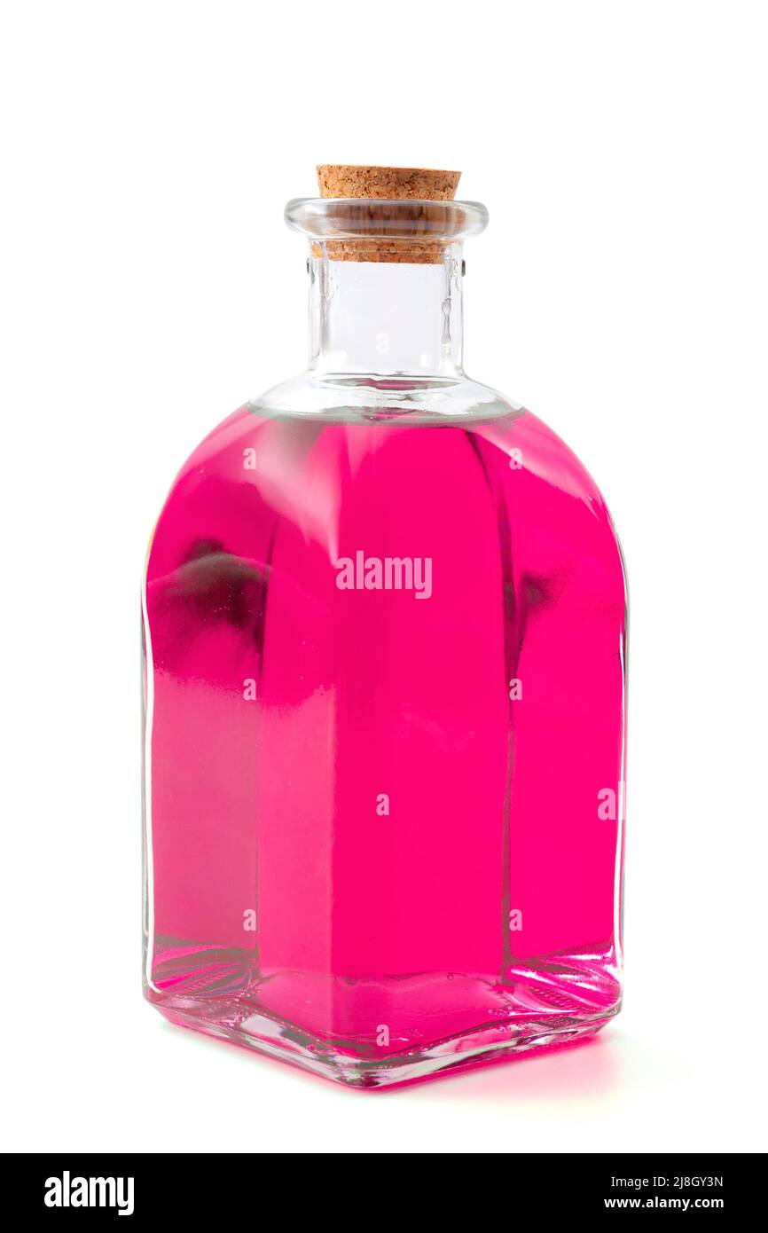 Hechizo mágico y poción, elixir apotecario o veneno mortal idea conceptual con una botella de vidrio vintage que contiene líquido rosa o púrpura aislado en el lugar Foto de stock