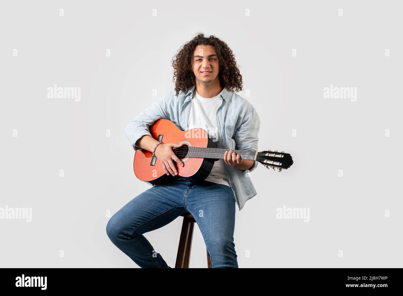 Hombre joven con pelo rizado, tocando guitarra acústica solo, aislado sobre fondo blanco. Fotografías de alta calidad Foto de stock