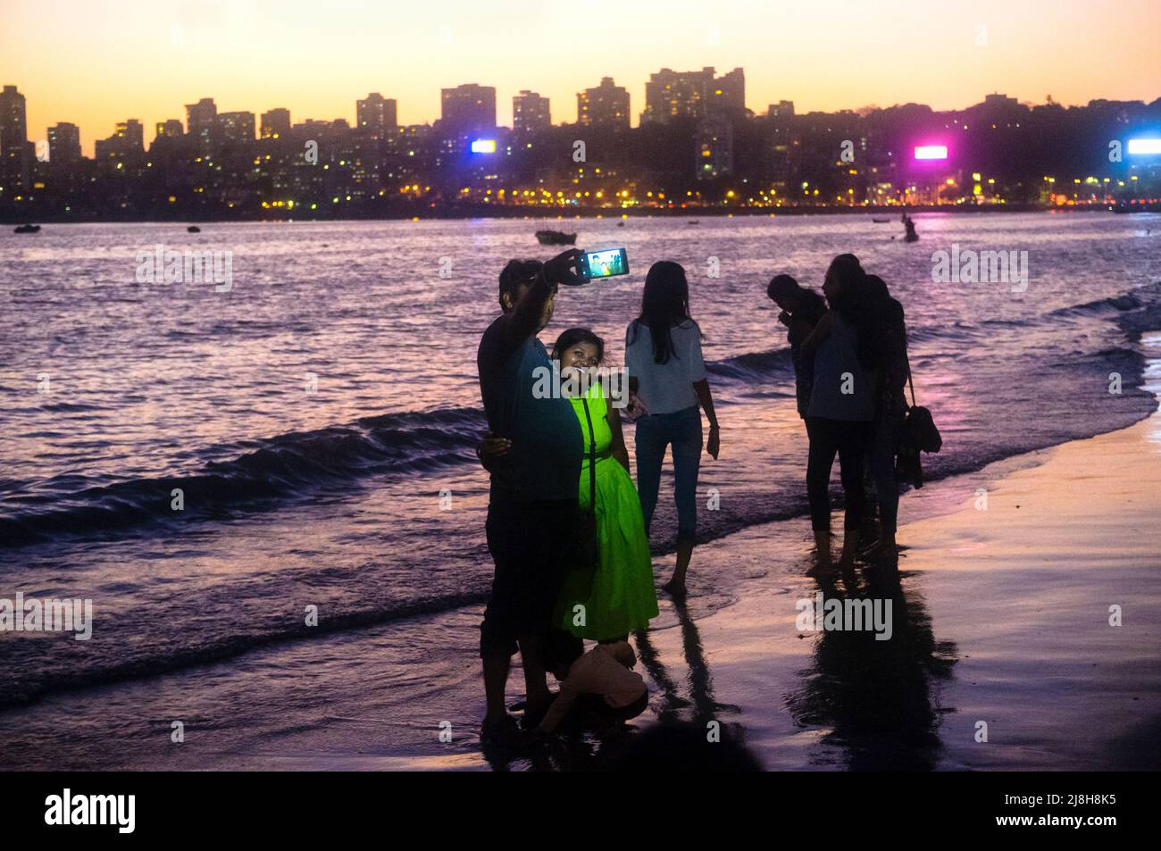 Mumbai, Maharashtra, India : La gente toma selfies al atardecer en la playa Girgaon Chowpatty. El barrio de Malabar Hill en el fondo es el más exclusivo de Mumbai Foto de stock