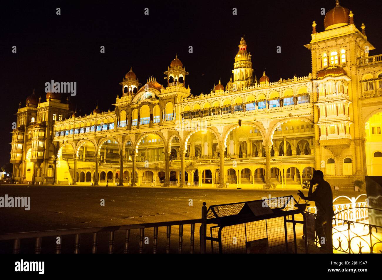 Mysore, Karnataka, India : Un guardia de seguridad se encuentra por la noche fuera del iluminado Palacio Mysore Maharaja. Foto de stock